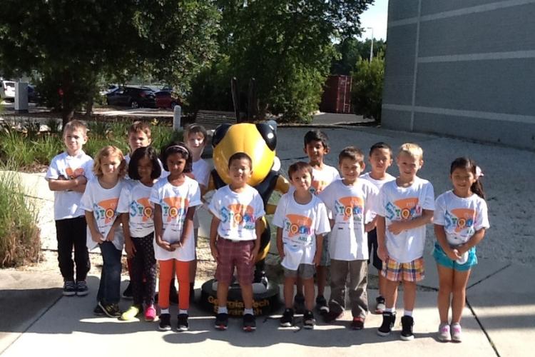 Small children part of K-12 camps stand in front of Buzz statue