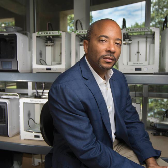 Raheem Beyah looking at camera thoughtfully as he sits in an additive manufacturing lab at Georgia Tech